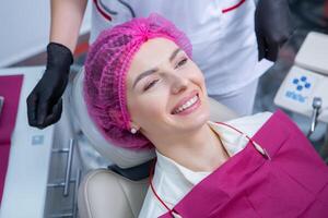 Portrait of young smiling woman sitting in stomatology clinic chair and doctor's hands with dental Mouth mirror and Dental explorer tools preparing to examine teeth condition. photo