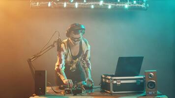 joven artista mezcla con tocadiscos en escenario, preparando a mezcla techno y disco música a tener divertido a Club nocturno fiesta. DJ ejecutante con loco maquillaje utilizando mezclador en mesa. trípode disparo. foto