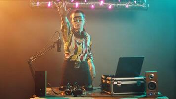 Cool musician presenting stop sign with palm raised, mixing modern sounds using headphones at turntables. Female DJ artist creating rejection and denial symbol at club. Tripod shot. photo