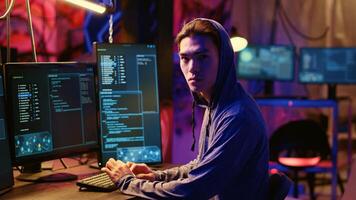 Portrait of asian hacker building spyware software designed to gather information from users computers without their knowledge. Man doing cybercriminal activities in rundown hideout photo