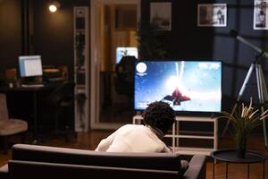Man playing entertaining spaceship videogame on smart TV, relaxing on living room couch. Player enjoying SF game on gaming console, shooting asteroids with laser beams using gamepad photo