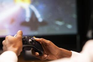 Close up shot of controller held by man playing galaxy flying videogame on smart TV, relaxing. Competitive gamer using joystick to have fun on gaming console in stylish apartment living room photo