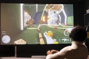 hombre en vivo habitación utilizando nube juego de azar Servicio a jugar exigente primero persona tirador videojuego en pantalla ancha televisor. jugador disfrutando alto calidad fps juego, disparo volador robots utilizando palanca de mando foto