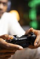 Focus shot on controller held by gamer in blurry background playing videogames. Close up shot of gamepad used by man enjoying gaming session in living room while sitting down in front of TV photo