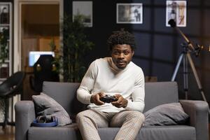 African american man playing videogame in home theatre, holding controller. Gamer participating in PvP online multiplayer game using console system and high quality gamepad photo