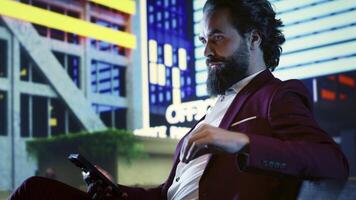 Banking expert reads digital investment news on phone while sitting on bench, admiring street lights downtown. Company shareholder in a suit trying to solve financial problems for CEO. photo