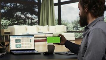 Wealthy businessman checks greenscreen on mobile phone layout, working to increase international profit from his opulent modern mansion in the woods. Entrepreneur uses blank copyspace display. photo