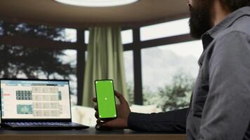 Adult millionaire looks at greenscreen smartphone display in his luxurious villa in the woods, wealthy company chief executive director. Entrepreneur uses blank mockup on phone, helping staff. photo