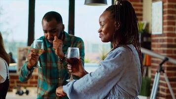 Cheerful friends dancing at house party while drinking wine glasses, enjoying weekend. Diverse group of people having fun indoors, doing dance moves to music in modern apartment living room photo