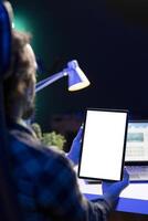 Over the shoulder view of a man grasping electronic tablet with blank chromakey mockup template. Young guy sitting at desk grasping digital device showing isolated white screen. photo