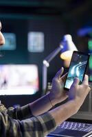 Male gamer sitting at desk and playing space shooter video games on smartphone. Man streaming online videogames for e-sport tournament on his mobile device while resting from work. photo