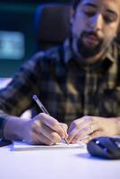 selectivo atención de masculino blogger escritura abajo nuevo ideas, planificación nuevo contenido. hombre sentado a mesa es utilizando un bolígrafo y cuaderno para escrito notas de su investigación trabajar. foto