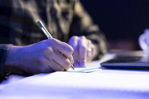 Selective focus on person writing on notepad at table, studying and researching of information. Closeup of an individual using pen to take down notes on paper, planning the day and completing tasks. photo