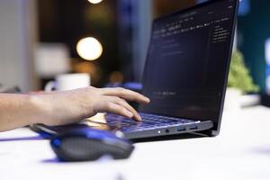 An individual is managing a system, typing on a keyboard while a laptop screen shows software programming. Person computing code, working on data center and network security. photo