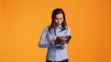 Filipino person navigating online on tablet over background, standing in studio and looking at internet pages on mobile device. Young adult holding gadget to text and browse websites. photo