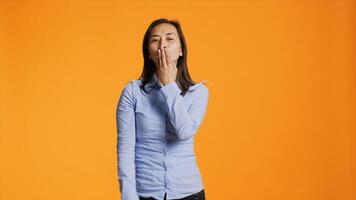 Flirty asian person blowing air kisses in studio, acting sweet with romantic gesture in front of camera. Young woman with casual clothes expressing love and sincere feelings. photo