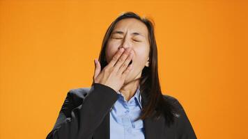 Exhausted person in formal clothes yawning and feeling sleepy in studio, trying to be awake and not fall asleep on camera. Young asian woman being tired and stressed, expressing burnout. photo