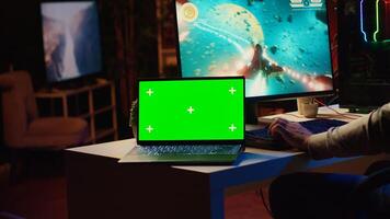 Mockup laptop next to man playing high FPS singleplayer videogame with spaceship shooting laser streams at asteroid. Green screen notebook near gamer using crosshair overlay to hit targets in SF game photo