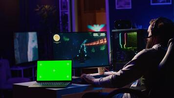 Green screen laptop next to man using gaming keyboard to play spaceship flying singleplayer game. Mockup notebook and gamer navigating with spacecraft in galaxy, shooting at asteroids photo