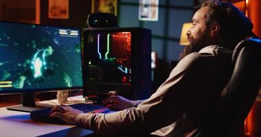 Man in neon lit apartment having fun and laughing while playing entertaining videogame, flying spaceship through galaxy. Pro gamer using desktop PC with powerful graphics to enjoy science fiction game photo