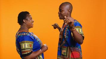 africano americano socios teniendo divertido bailando en estudio, disfrutando su favorito canción y demostración romántico lento danza se mueve étnico casado Pareja escuchando a frio canciones terminado naranja antecedentes. foto