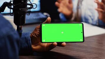 Close up shot of green screen phone hold by man invited to podcast watching internet clips in apartment studio. Chroma key smartphone running videos for podcasters to react to photo