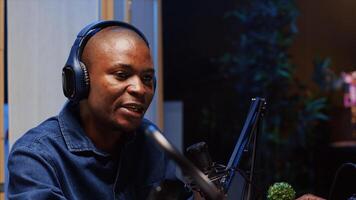 African american man doing podcast in studio, wearing headphones and talking on professional microphone with guest. Close up shot of BIPOC content creator interviewing another person photo