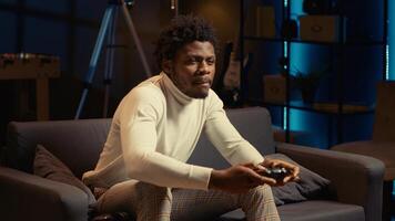 Energetic african american man playing videogames on couch, using spamming buttons on motion controlled controller. Player battling opponents in internet multiplayer game on console photo