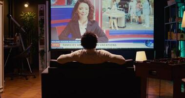 Man in home theatre watching huge TV screen showing news broadcast reportages on family trips. Zoom in shot on cord cutter looking at streaming service travelling channel on widescreen television set photo