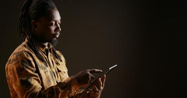 Model holding mobile tablet to check websites over black background, using device to browse through social media pages and connect with his friends. African american man on internet network. photo