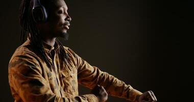 African american guy listens to cool music on headset and having fun in studio, dancing over black background. Confident trendy person shows groovy dance moves, good songs on headphones. photo