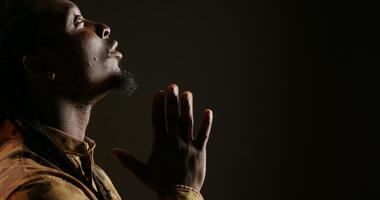 Religious adult believing in Jesus and praying in studio, showing belief and being hopeful over black background. Spiritual man feeling optimistic and talking to God. Handheld shot. Close up. photo