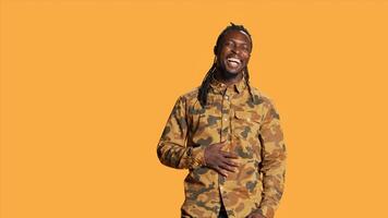 Cheerful adult enjoying shoot and laughing on camera, making jokes in studio and acting playful. Silly positive african american guy having fun over orange background, relaxed casual person. photo