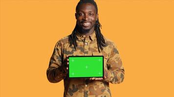 Male model holding laptop with greenscreen layout in studio, posing with isolated display copyspace on pc. Young adult presenting computer with blank mockup template on camera. photo