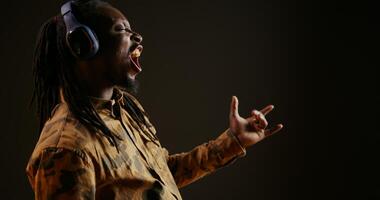 Cool person playing air guitar and listening to music on camera, pretending to play imaginary instrument and create tunes. African american man having fun with songs on headset, musical activity. photo