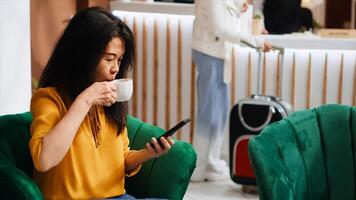 Hotel guest waiting for check in process at hotel, using phone to scroll on social media and pass time. Asian woman arriving early at five star resort, relaxing after long flight. photo