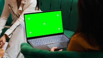 Hotel guest using laptop with greenscreen layout in lobby, looking at copyspace chromakey display in lounge area. Modern person holding pc showing isolated mockup template on screen. photo