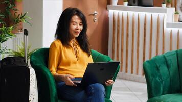 Asian hotel guest on videocall with family members, talking to people after arriving at hotel. Young adult using laptop connection network for videoconferencing remotely, holiday trip. photo