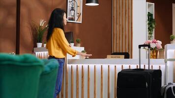 Asian guest arriving at front desk and ringing service bell to receive assistance for accommodation, calling for receptionist to do check in process. Woman talking to hotel staff. Handheld shot. photo