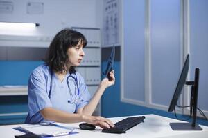 A female physician works long hours in a hospital office analyzing radiographs and typing medical knowledge. Young practitioner planning medication therapy to aid in patient recovery from illness. photo