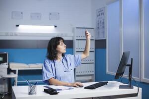 A young physician grasping an X-ray image and typing notes on her computer. A female Caucasian healthcare professional is shown in the photograph examining a chest scan of a patient. photo