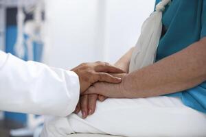 Close-up shows doctor supporting senior patient at clinic office by holding their hands. Medical professional assisting old person with chiropractic examination and diagnosis. photo