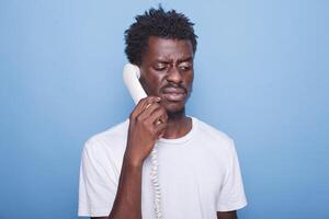 de cerca de africano americano hombre teniendo un teléfono llamada conversacion con un irritado expresión. negro chico participación un teléfono fijo teléfono cable a su oído para comunicación con amigos. foto