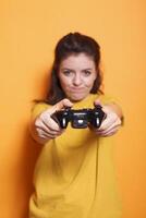 Close-up of female gamer using joystick on console in front of camera. Focused woman holding controller and playing video games with technology, standing over isolated background. photo