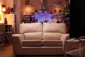 Empty living room with modern furniture ready for christmas holiday. In background x-mas decorated kitchen during winter season waiting for guest. Stylish christmas ornaments. December decorations photo
