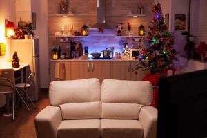 Empty xmas living room with nobody in it ready for winter holiday at home. In background x-mas decorated kitchen with modern furniture. Christmas ornaments at home. December festive decorations photo