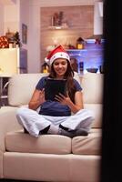 Girl person relaxing in xmas decorated kitchen sitting in lotus position on sofa browsing social media using tablet computer. Woman searching x-mas holiday celebrating winter season photo