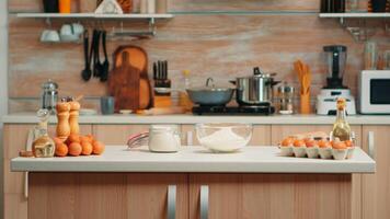 Pastry ingredients for homemade cakes and bread in empty kitchen. Modern dining room equipped with utensils ready for cooking with wheat flour in glass bowl and fresh eggs on table photo