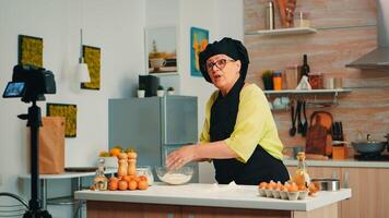 Woman baker presenting recipe while recording tutorial for social media. Retired blogger chef influencer using internet technology communicating, shooting, blogging on podcast with digital equipment photo