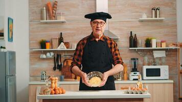 Old man wearing bonete while explaining food preparation recipe looking at camera. Retired blogger chef influencer using internet technology communicating on social media with digital equipment photo